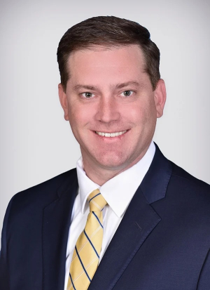 Man wearing a yellow tie and blue blazer smiles in a posed photo 