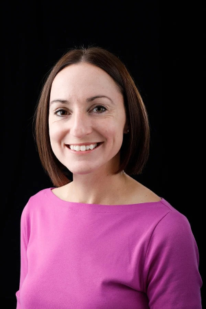 Women in a magenta shirt has dark brown hair and smiles 