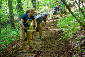 Group of people using rakes and other tools clear a trail in a natural trail area.