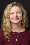 Woman with long, curly blonde hair smiles while wearing a maroon sweater