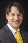 Man wearing a suit with a yellow tie smiles 